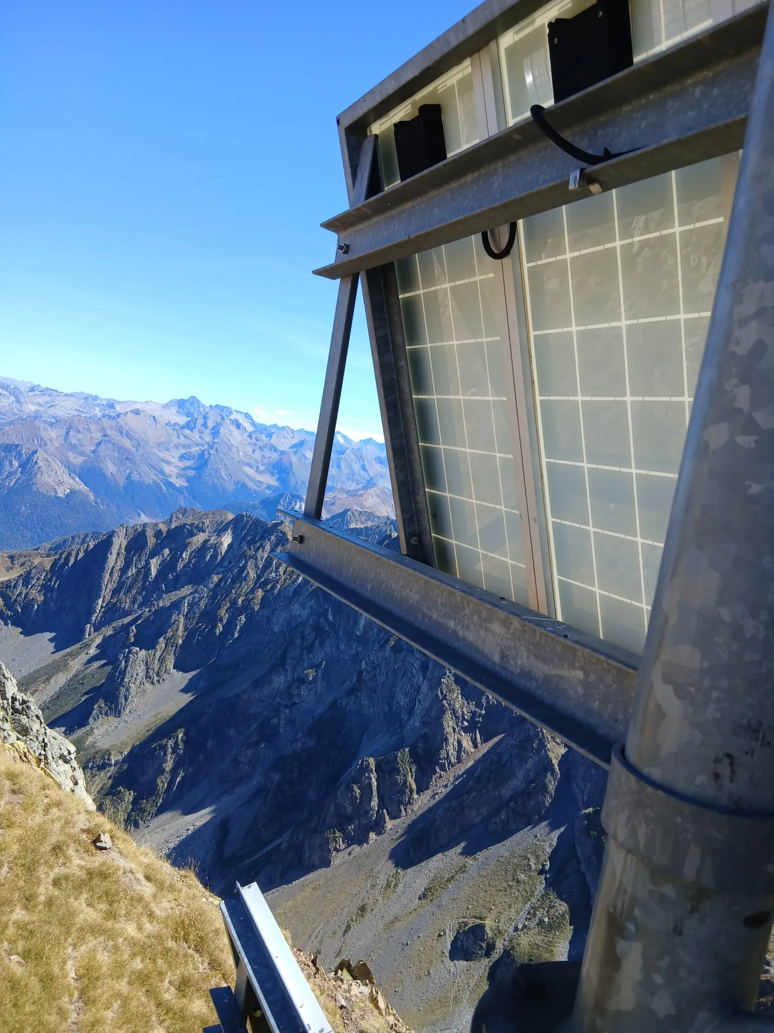Panneaux solaires posés au sol et cabanon technique au pied d’une montagne basque
